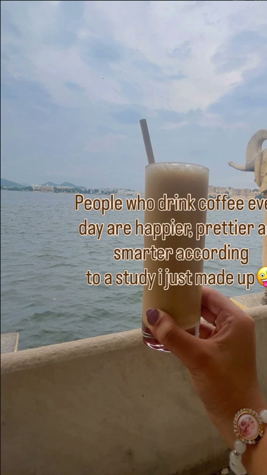 Iced coffee held up against Lake Pichola in Udaipur